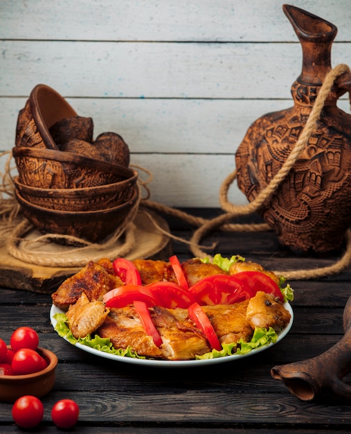 poulet grillé garni de tranches de tomate sur des feuilles de laitue