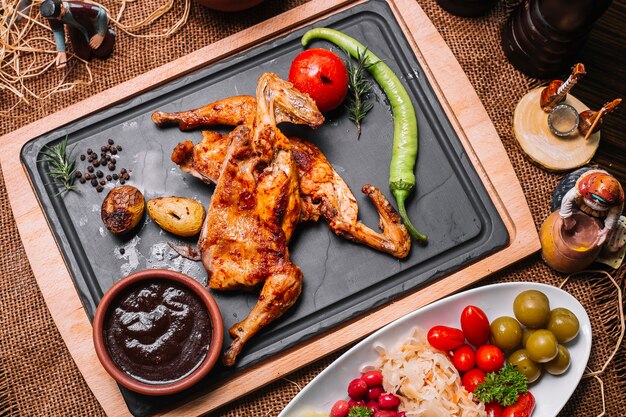 Poulet grillé sur planche de bois avec sauce tomate pomme de terre poivron cornichons vue de dessus