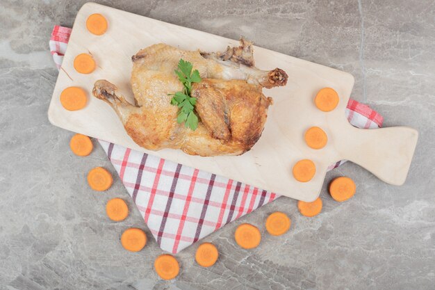 Poulet grillé sur planche de bois avec des tranches de carottes.