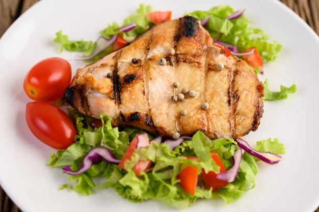 Poulet grillé sur une plaque blanche avec une salade de tomates, carottes et piments coupés en morceaux.