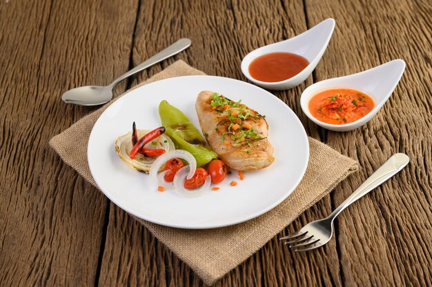 Poulet grillé sur une plaque blanche avec tomates, salade, oignon, piment et sauce.