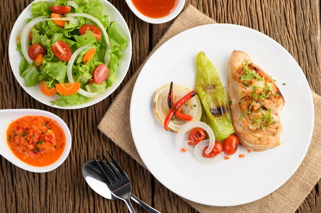 Poulet grillé sur une plaque blanche avec tomates, salade, oignon, piment et sauce.