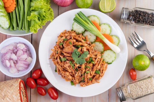 Poulet haché épicé sur une assiette blanche avec concombre, laitue et accompagnements.