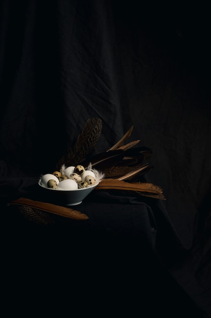 Poulet et oeufs de caille entre les plumes dans un bol près de grosses piquants