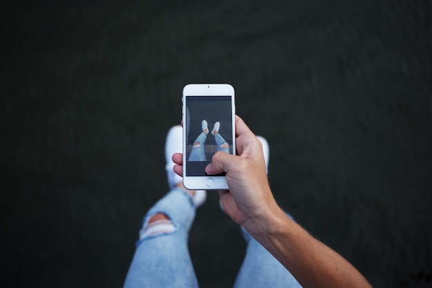 POV d'un homme en jean skinny hipster à la mode à la mode faisant des photos de ses jambes et de ses pieds en baskets blanches sur smartphone pour les médias sociaux