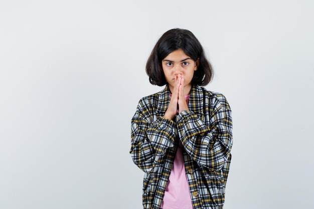 Préadolescente en chemise, veste tenant les mains combinées sur la bouche tout en attendant des nouvelles et en regardant patient, vue de face.