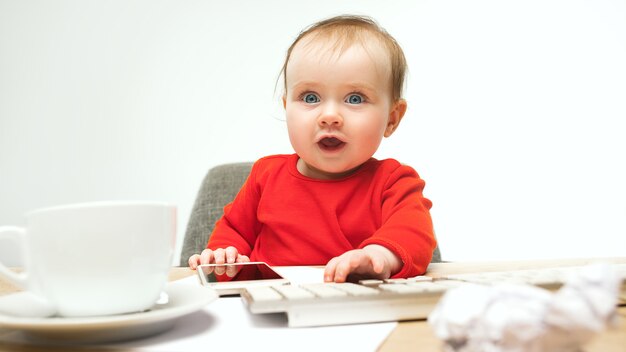 Premier sms. Enfant bébé fille assise avec clavier d'ordinateur moderne ou ordinateur portable en blanc