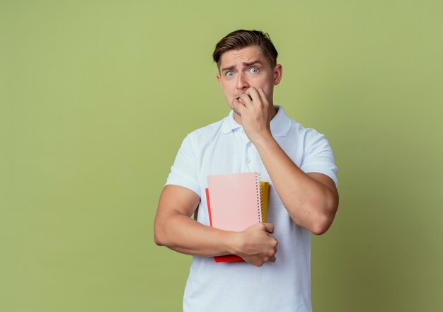 Préoccupé jeune beau étudiant masculin tenant des livres et mord les ongles isolés sur fond vert olive