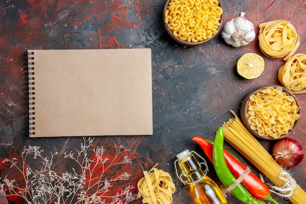 Préparation du dîner avec des pâtes non cuites piments de Cayenne attachés les uns aux autres avec une bouteille d'huile de corde ail citron et cahier sur des images de table de couleurs mélangées