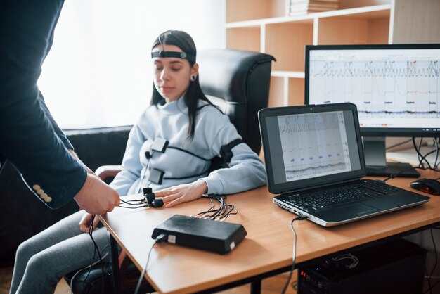 Préparation, pose d'électrodes sur les doigts. La fille passe le détecteur de mensonge dans le bureau. Poser des questions. Test polygraphique