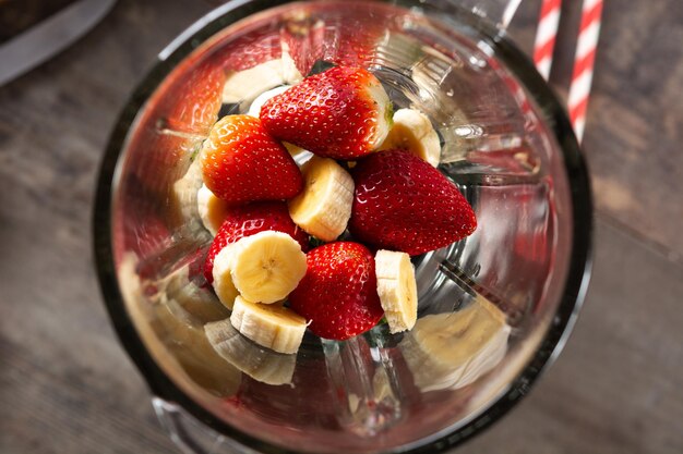 Préparation d'un smoothie aux fraises et à la banane dans un mixeur sur une table en bois