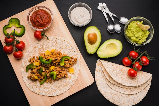 Préparation de tacos sur une planche à découper près de légumes et de sauces