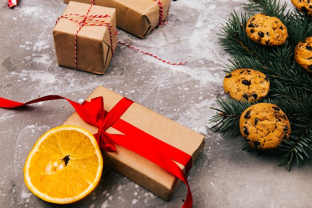 Présent boîte avec ruban rouge se trouve sur le sol gris avant la branche de sapin avec des cookies