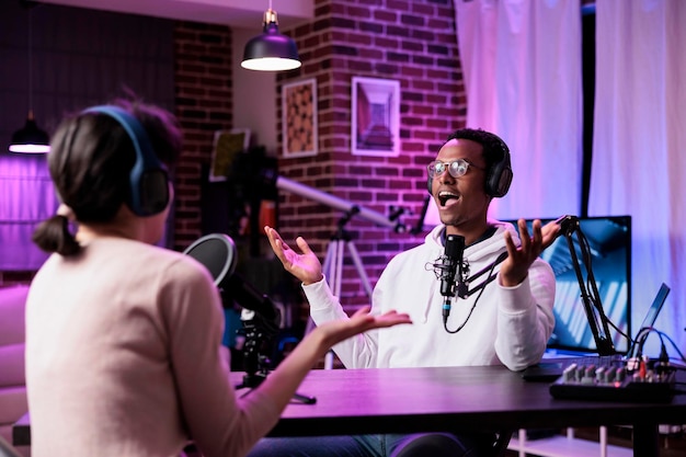 Présentateur de podcast enregistrant un chat en direct à la station de production, utilisant un équipement moderne pour le public. Influenceur masculin interviewant une femme pour une discussion diffusée en ligne en studio.
