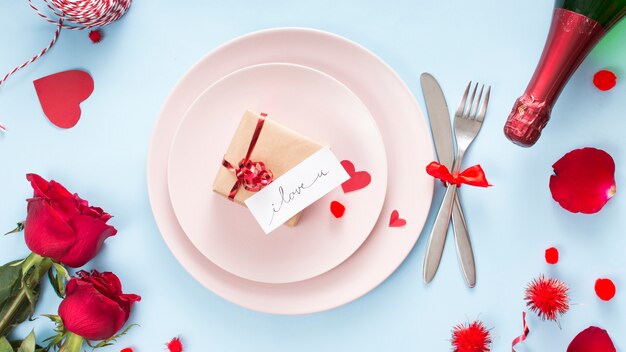 Présenter avec du papier sur une assiette près des couverts, des roses et une bouteille de champagne