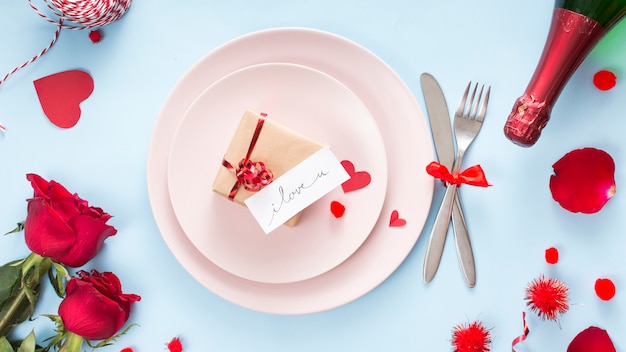 Présenter avec du papier sur une assiette près des couverts, des roses et une bouteille de champagne