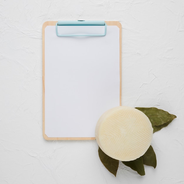 Photo gratuite presse-papiers vierge avec du manchego espagnol et des feuilles de laurier séchées sur fond de béton blanc