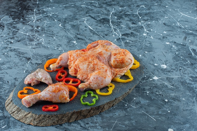 Prêt à cuire la viande de poulet et le poivre sur une planche, sur le fond bleu.