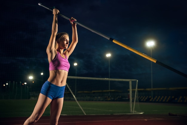 Prêt à surmonter les difficultés. Formation professionnelle de saut à la perche féminine au stade le soir. Pratiquer à l'extérieur. Notion de sport