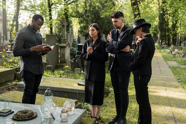 Prêtre masculin lisant de la bible à la tombe avec la famille de deuil