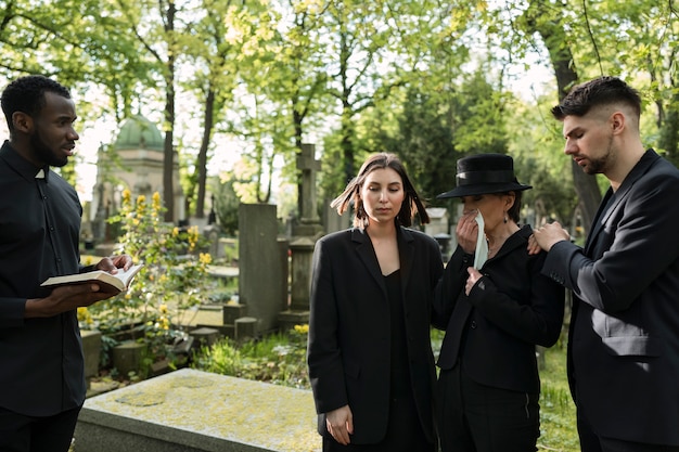 Prêtre masculin lisant de la bible à la tombe avec la famille de deuil