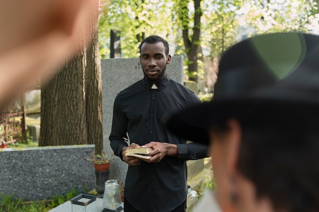 Prêtre masculin lisant de la bible à la tombe avec la famille de deuil