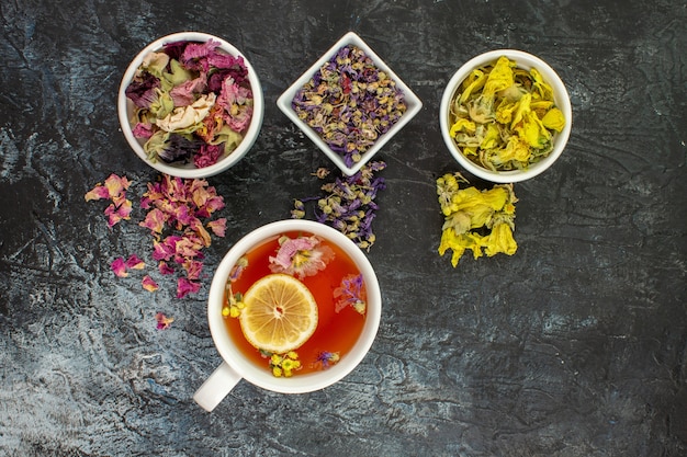 Photo gratuite prise de vue aérienne d'une tasse de tisane avec des bols de fleurs sèches sur fond gris