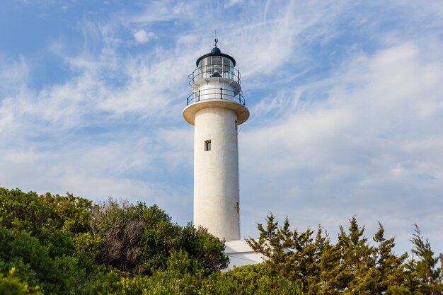 Prise de vue en contre-plongée d'un phare avec un ciel bleu nuageux vu à travers les arbres