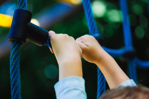 Prise de vue à faible angle d'un enfant se tenant à un jouet d'escalade bleu sur l'aire de jeux d'un parc