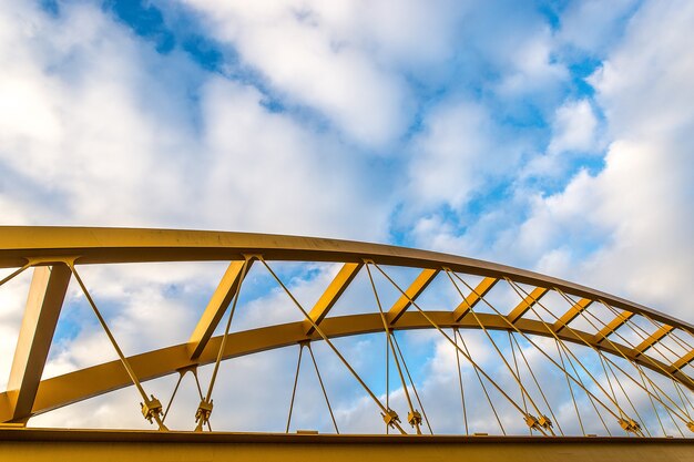 Prise de vue à faible angle d'un pont à haubans jaune avec un ciel bleu nuageux