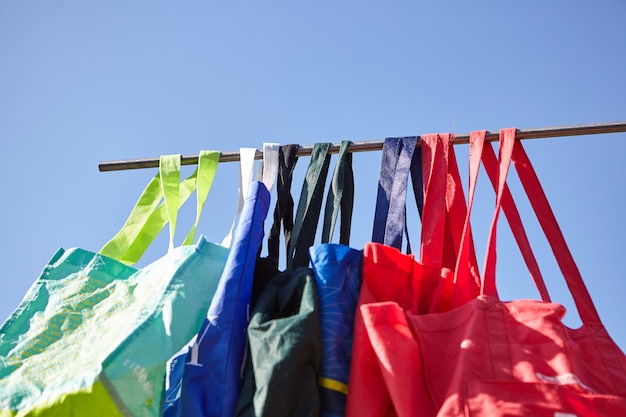 Photo gratuite prise de vue à faible angle de sacs en tissu réutilisables écologiques colorés suspendus sur un poteau - pas de concept en plastique