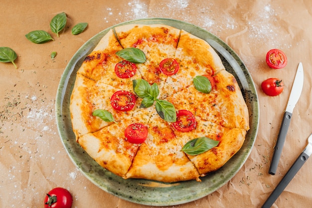 Prise de vue en grand angle d'une délicieuse pizza avec des tranches de tomate et de feuilles de basilic