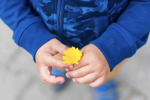 Prise de vue en grand angle d'un enfant tenant une fleur jaune
