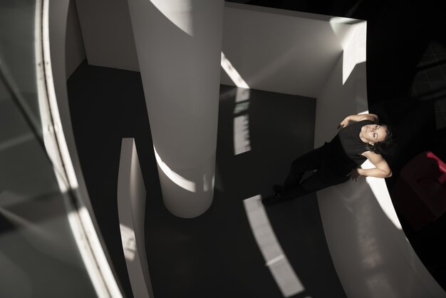 Prise de vue en grand angle d'une femme appuyée sur un mur blanc dans un immeuble avec un sol noir