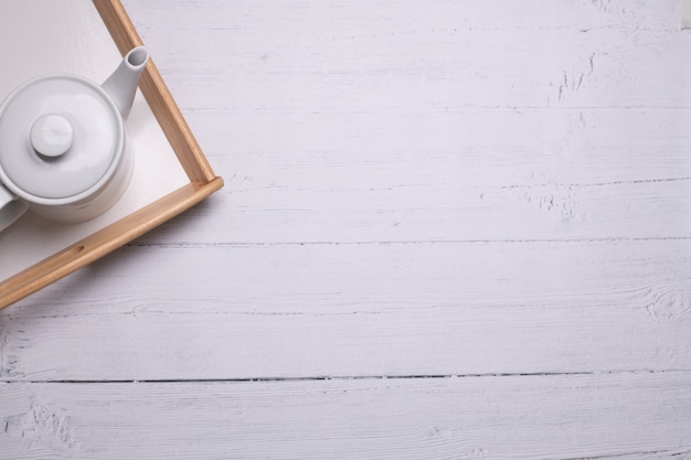 Prise de vue en grand angle d'une théière blanche sur un plateau sur une table en bois blanc