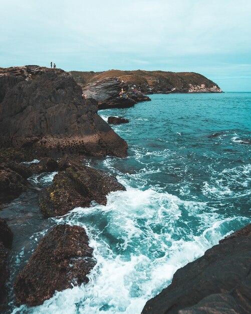 Prise de vue en grand angle des vagues de la mer frappant les rochers avec un ciel nuageux