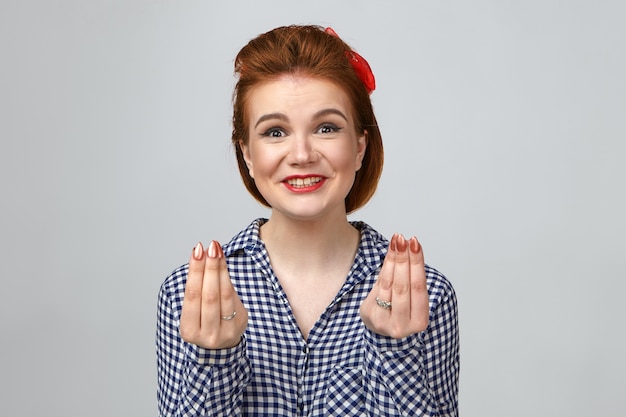 Prise de vue horizontale en studio d'une jeune femme européenne glamourore émotionnelle drôle avec une coiffure élégante et un maquillage lumineux s'exclamant avec enthousiasme, tenant les doigts comme si comptant de l'argent, profitant d'une grande vente