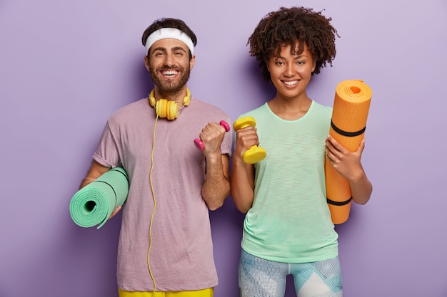 Prise de vue à l'intérieur d'une femme et d'un homme motivés heureux, s'entraînent quotidiennement dans une salle de sport, travaillent sur les biceps, soulèvent des haltères