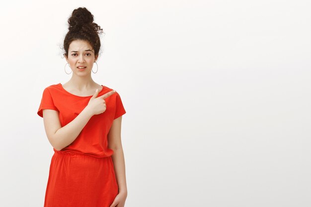 Prise de vue à l'intérieur d'une femme séduisante non impressionnée mécontente en jolie robe, pointant vers le coin supérieur droit avec une expression de déception douteuse