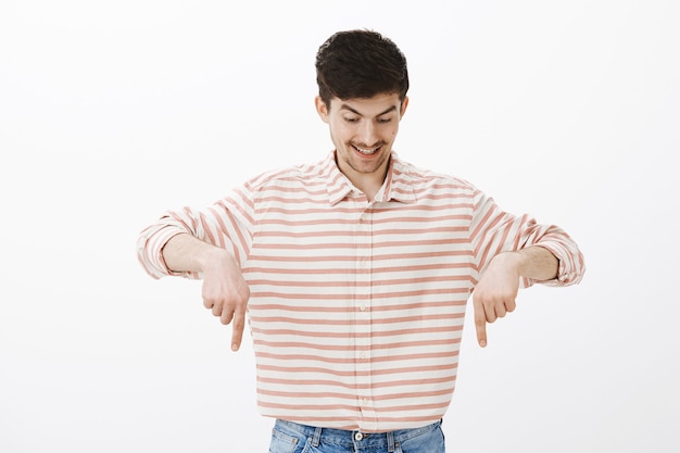 Photo gratuite prise de vue à l'intérieur d'un jeune modèle masculin étonné heureux avec barbe et moustache, pointant et regardant vers le bas avec un sourire heureux, surpris et excité de voir des poissons intéressants pendant le voyage en bateau