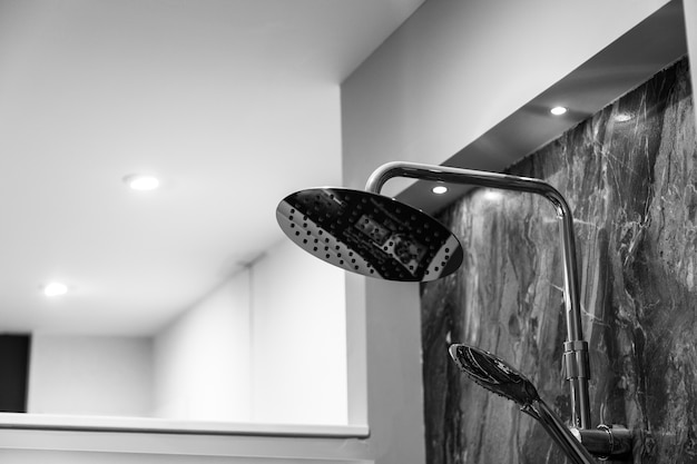 Prise de vue en niveaux de gris d'une douche attachée à un mur de marbre dans une salle de bains