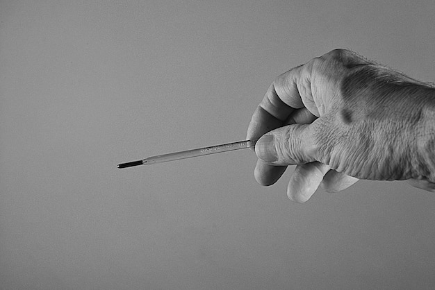 Prise de vue en niveaux de gris d'un thermomètre entre les mains d'un médecin pour la prévention du coronavirus