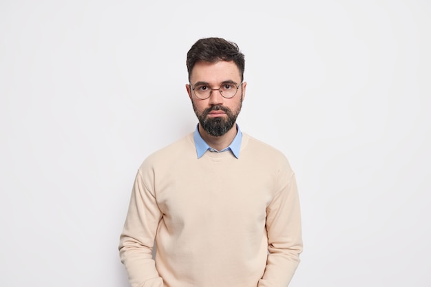 Prise de vue en studio d'un bel homme européen adulte barbu regarde directement, avec une expression sérieuse a déterminé le visage vêtu de lunettes rondes de cavaliers soignées