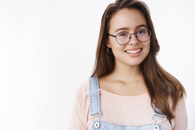 Prise de vue en studio d'une fille heureuse portant de nouvelles lunettes prescrites souriant comme aimant de nouvelles montures soulagée de voir clairement debout heureux et ravi sur fond gris avec un large sourire