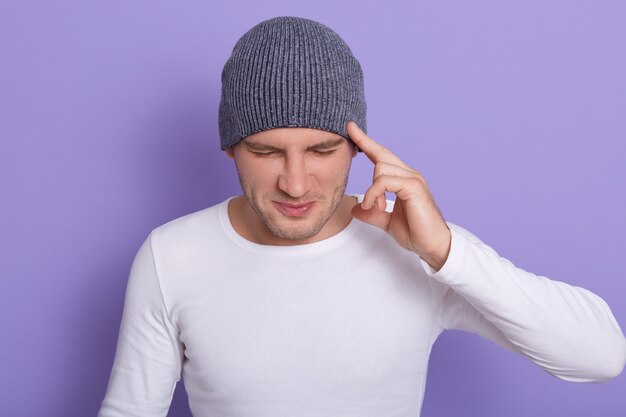 Prise de vue en studio d'un homme séduisant avec les yeux fermés, garde le doigt sur les tempes, a de terribles maux de tête ou oublie quelque chose d'important