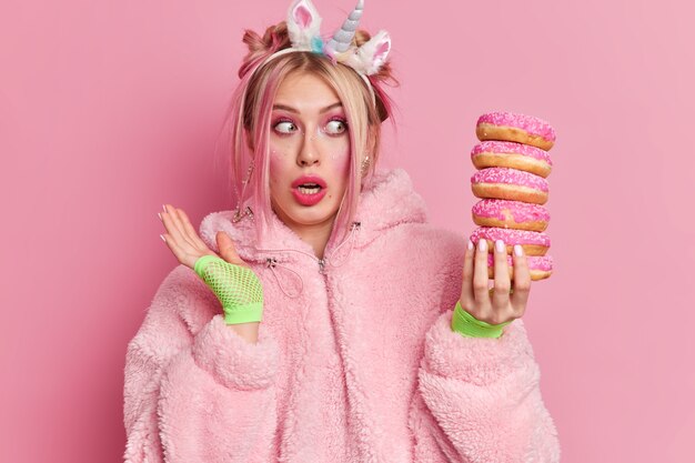 Prise de vue en studio d'une jeune femme européenne choquée regarde avec surprise une pile de beignets se rend compte de la quantité de calories qu'il contient