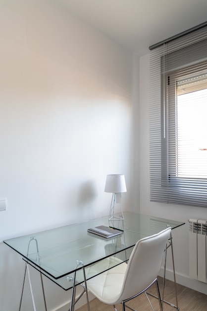 Prise de vue verticale à grand angle d'une salle blanche minimaliste avec un bureau en verre près de la fenêtre