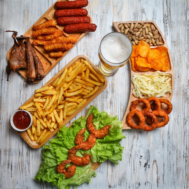 Produits de malbouffe avec bière, fromage, barbecue, pistache dans des assiettes en bois