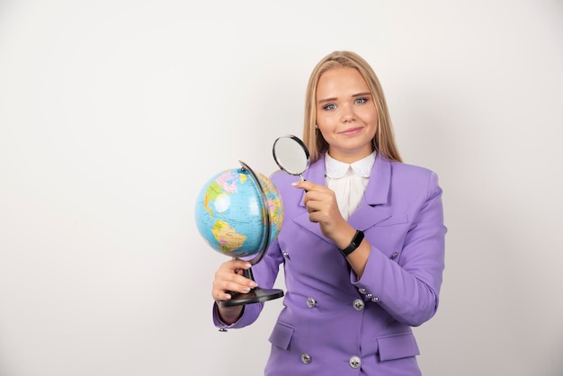 Professeur blonde regardant globe avec loupe. Photo de haute qualité