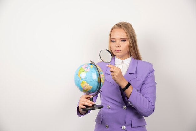 Professeur de femme regardant le globe avec une loupe avec une expression sérieuse.